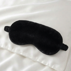 black luxury faux fur sleep mask with satin lining on white silk background