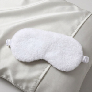 Pure white luxury faux fur sleep mask with satin lining on white silk pillow