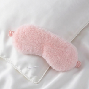 Blush pink luxury faux fur sleep mask with satin lining on white silk pillow